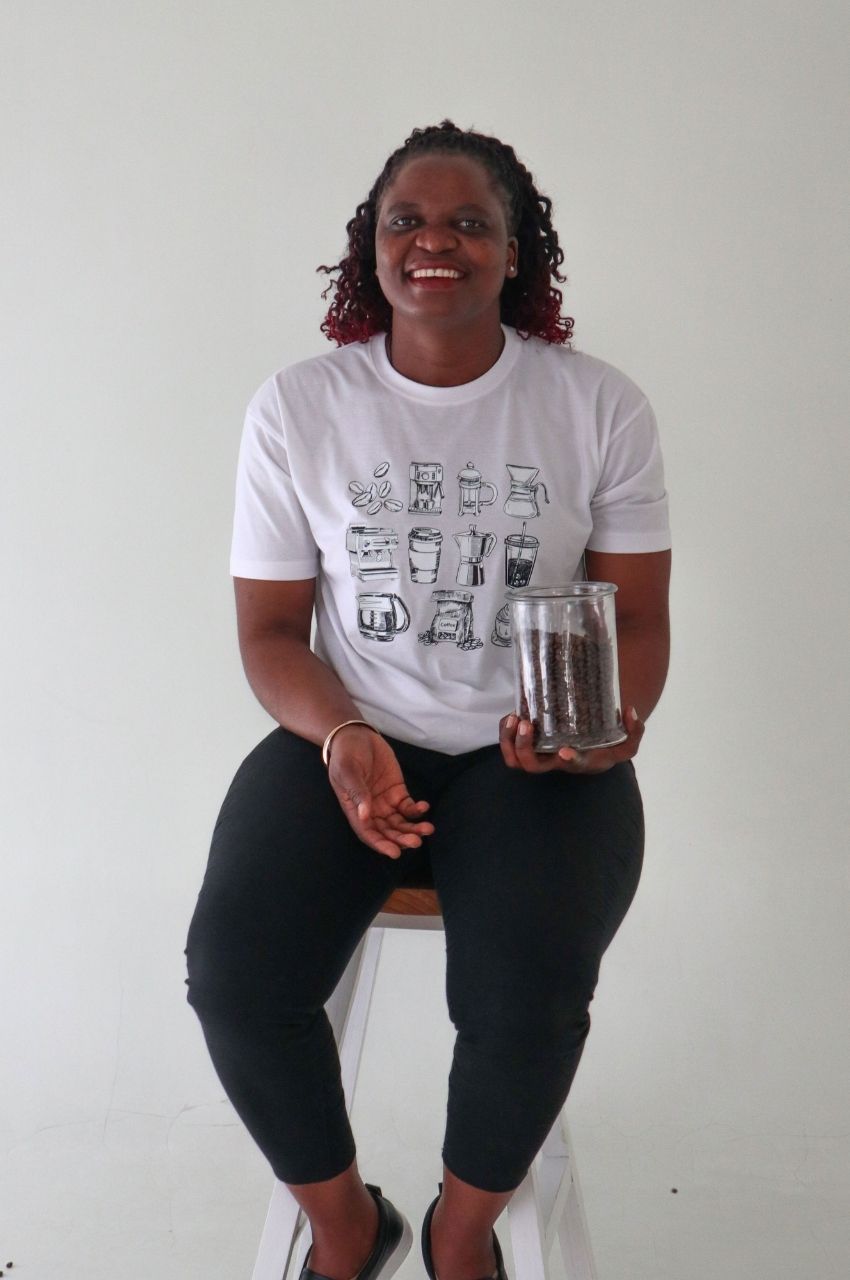 Woman wearing white t-shirt with coffee brewing illustrations holding coffee beans South Africa