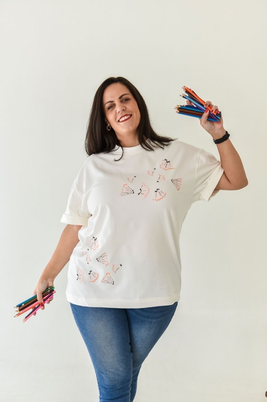 Woman wearing white t-shirt with pencil shaving artwork design holding colored pencils South Africa