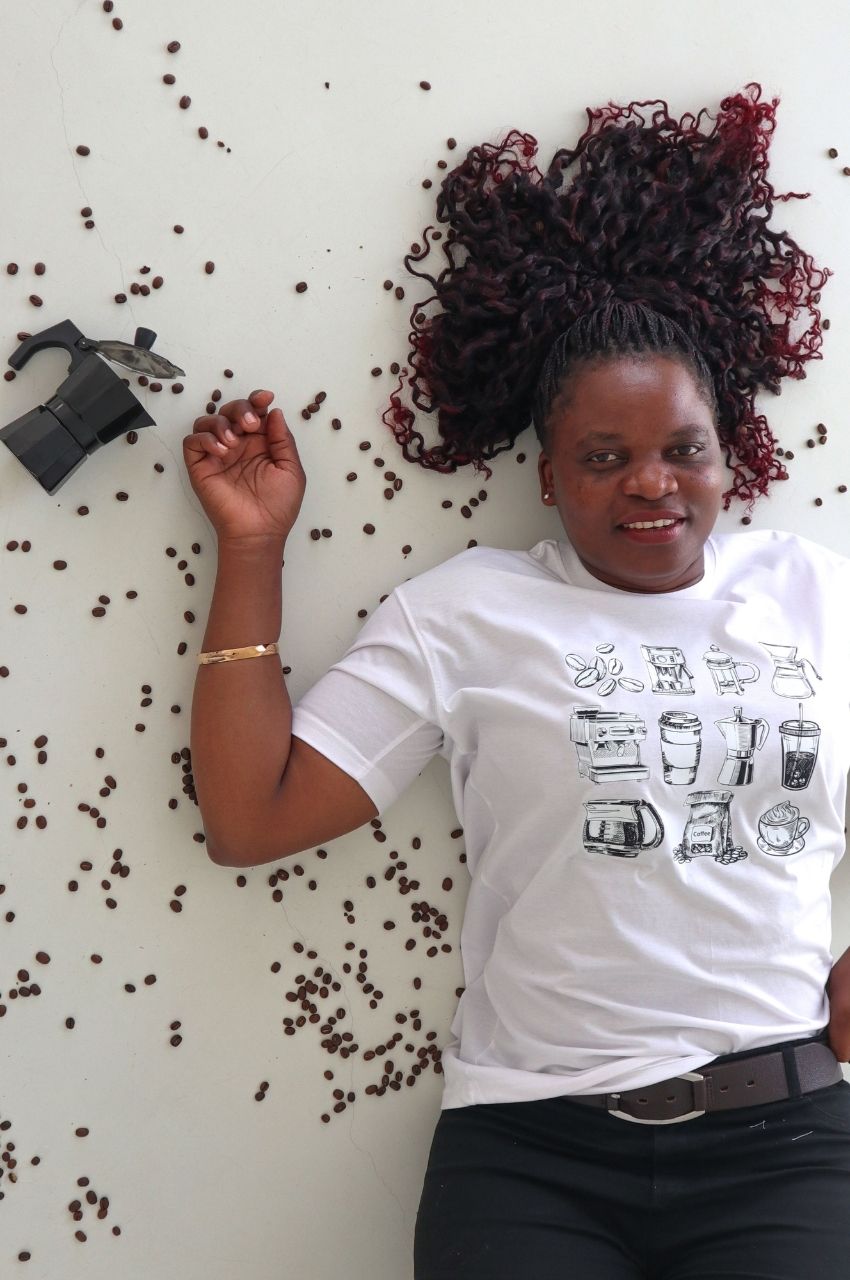 Woman lying with coffee beans and moka pot wearing white t-shirt with coffee illustrations South Africa