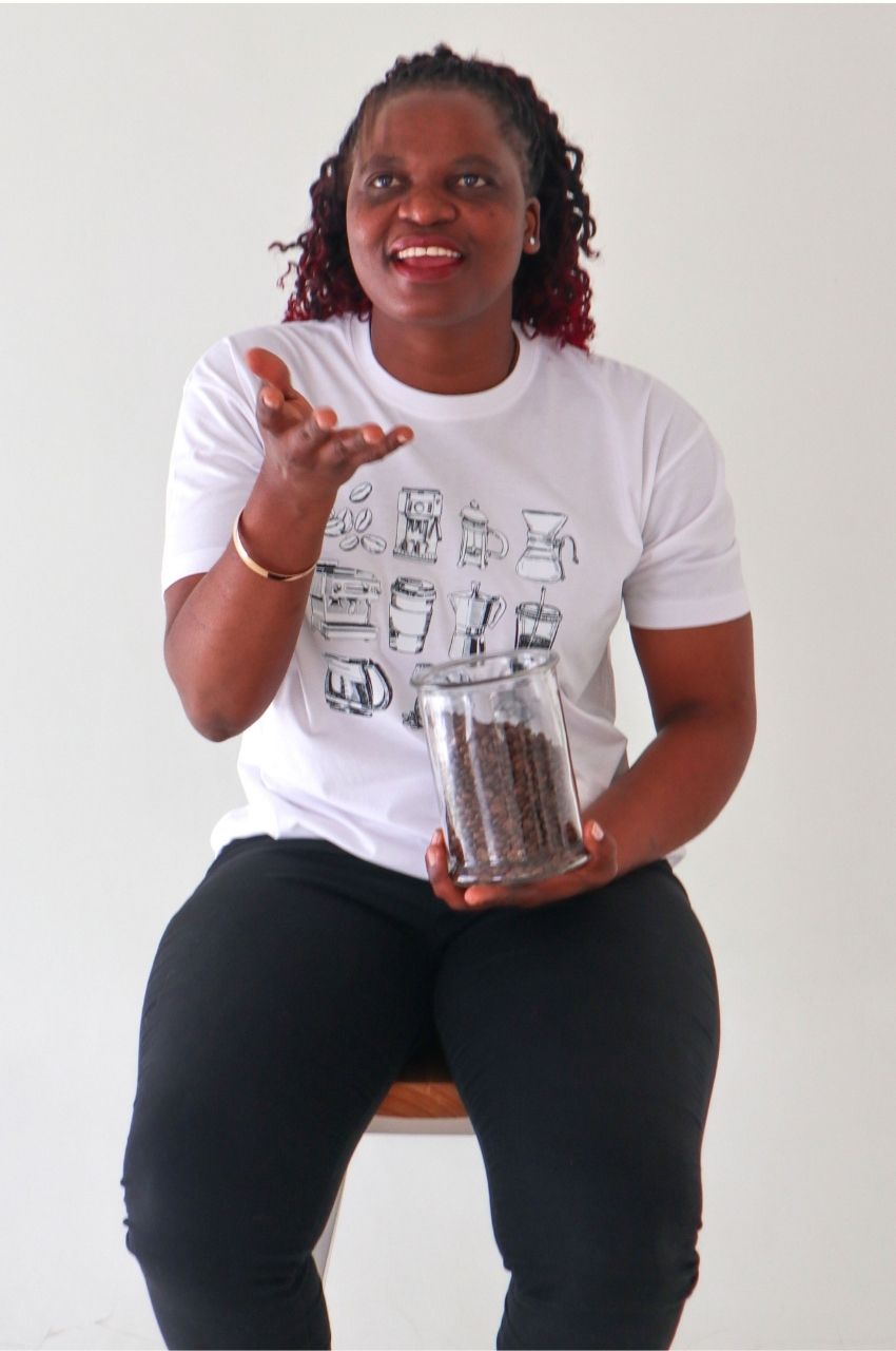 Woman holding coffee beans wearing white t-shirt with coffee brewing design playful lifestyle South Africa