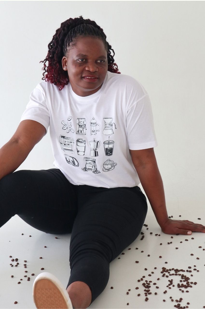 Woman sitting with scattered coffee beans wearing white t-shirt with coffee equipment graphic South Africa