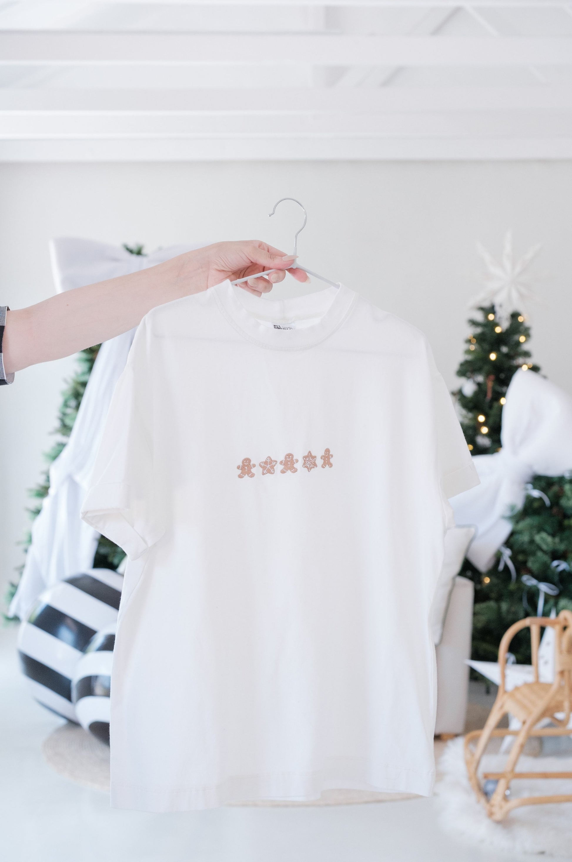 White minimalist Christmas t-shirt with small gingerbread embroidered design hanging on hanger South Africa