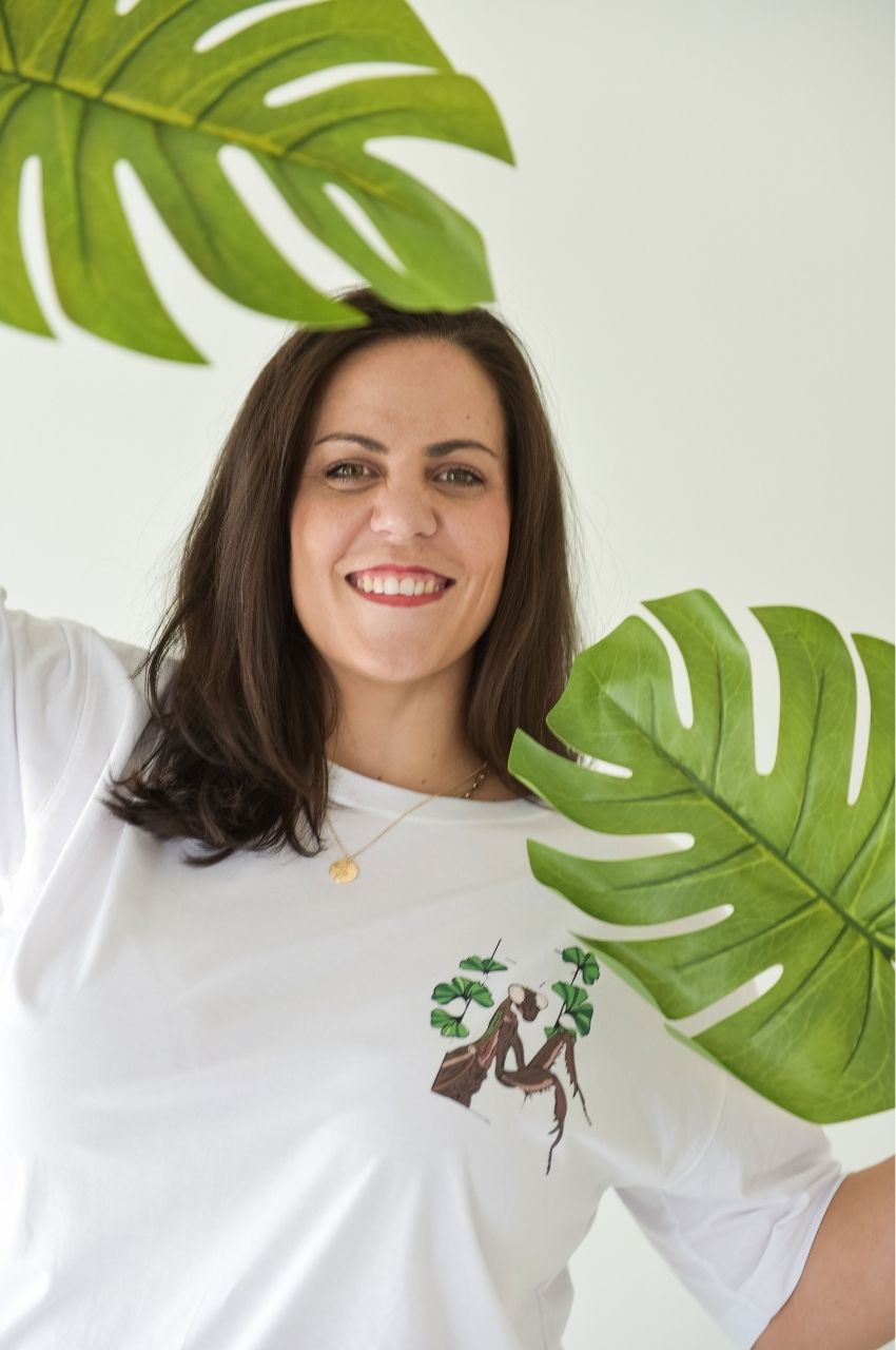 Close up of white t-shirt with small tree and figure illustration surrounded by green leaves South Africa