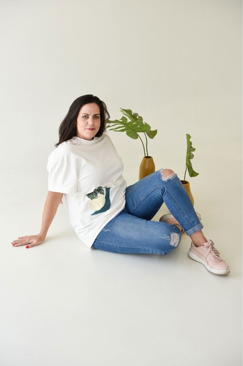 Woman sitting wearing white t-shirt with snail plant graphic paired with jeans casual outfit South Africa