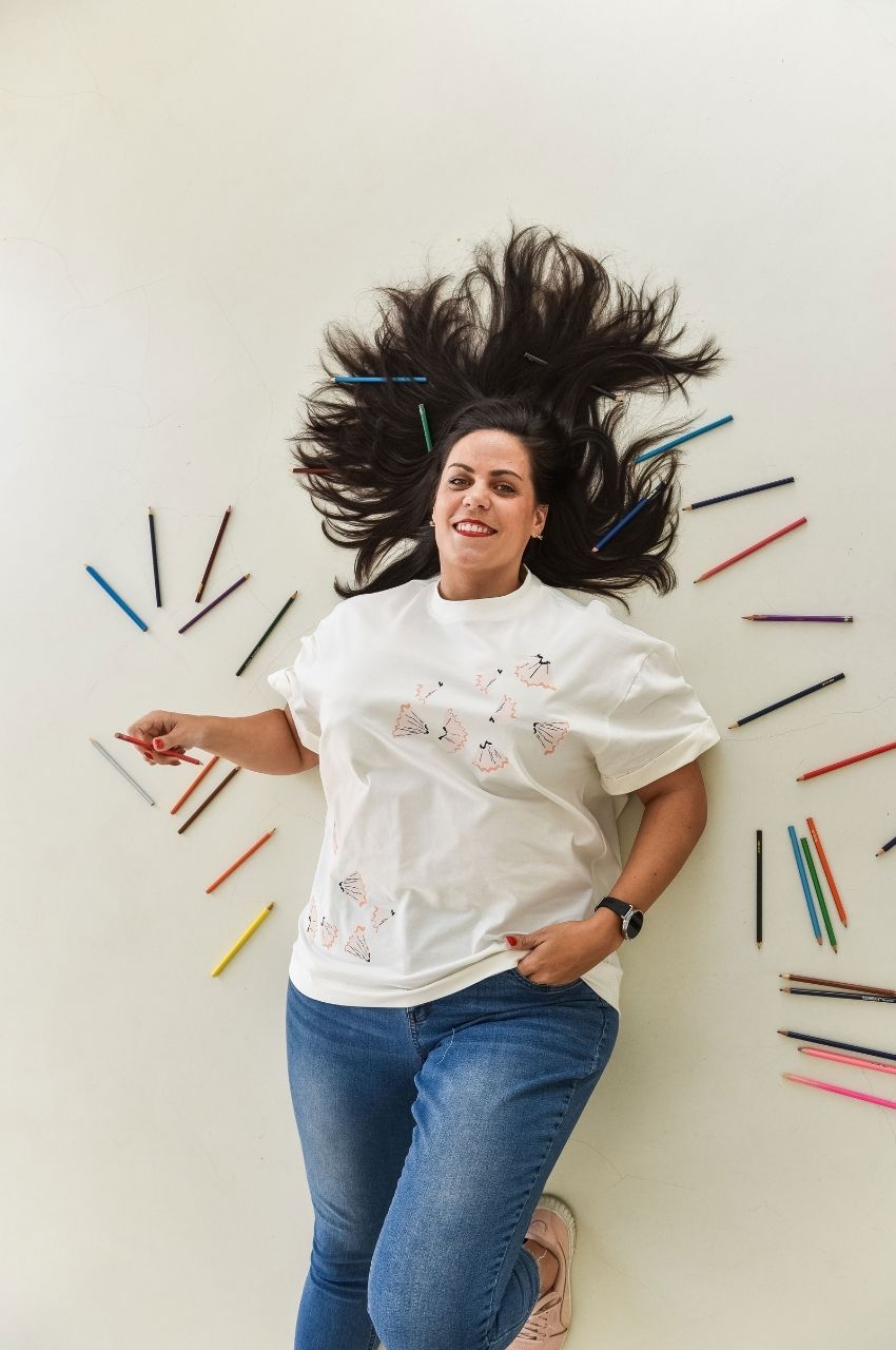 Woman lying with colored pencils wearing white t-shirt with pencil shaving graphic creative design South Africa