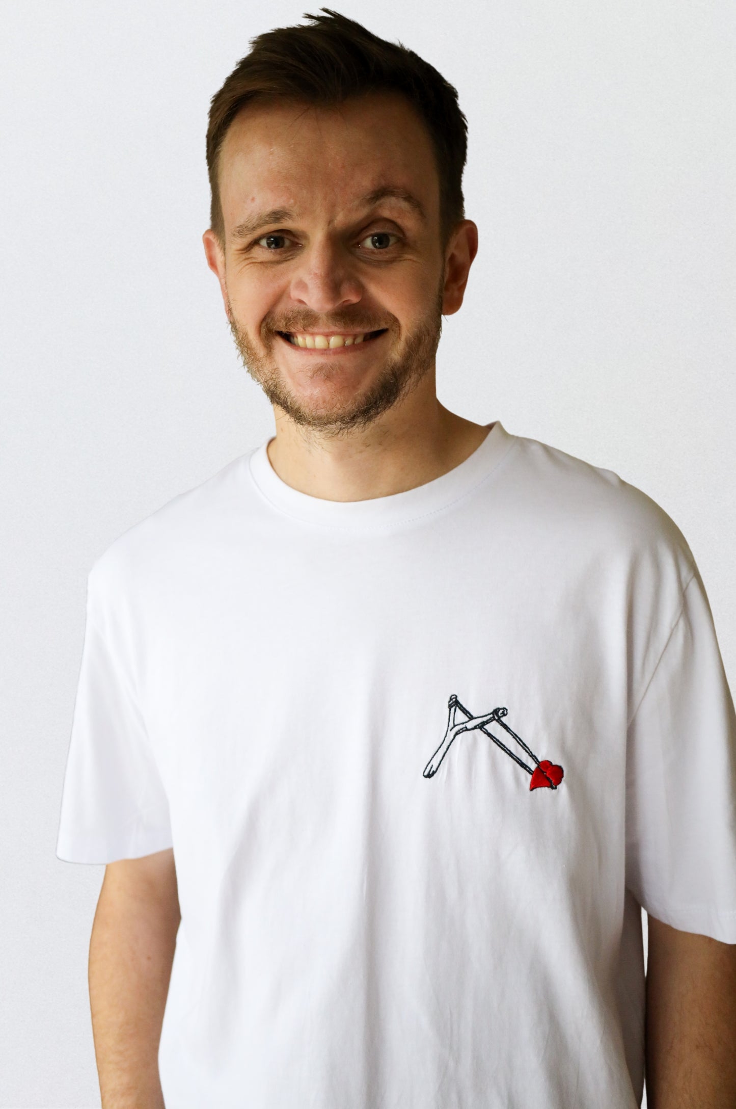 Man wearing white graphic t-shirt with embroidered slingshot heart design, 100% cotton quirky tee South Africa