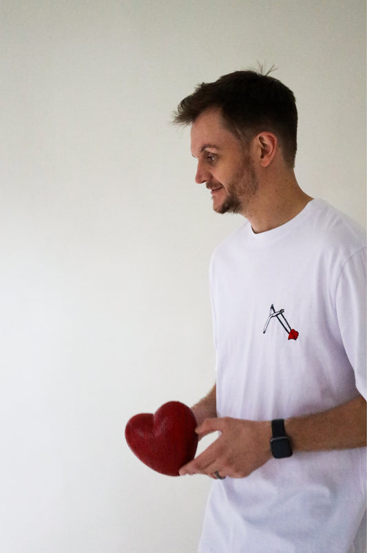 Man wearing a white graphic t-shirt with embroidered slingshot and red heart design, 100% cotton quirky t-shirt made in South Africa