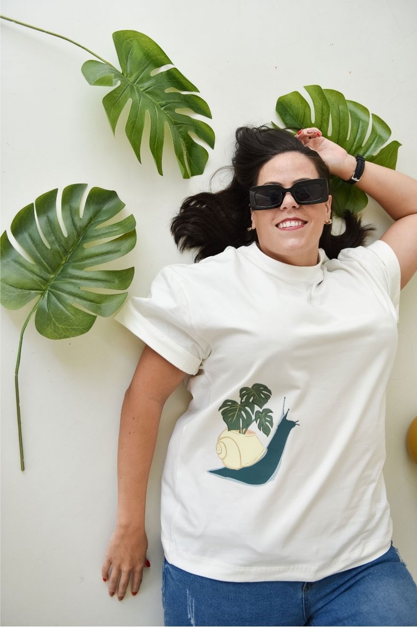 Woman lying with green leaves wearing white t-shirt with snail and monstera plant design aesthetic shirt South Africa