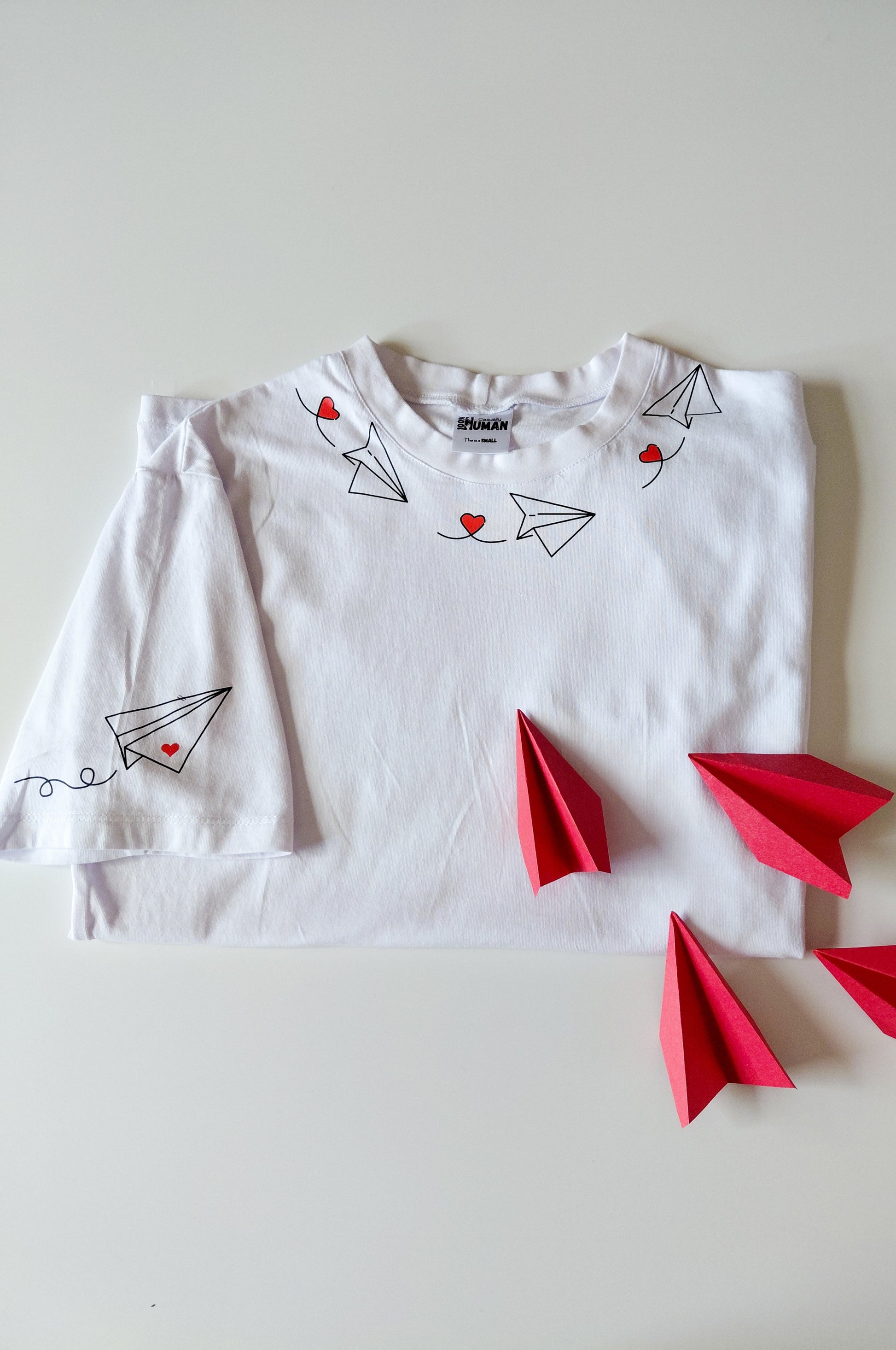 White graphic t-shirt with paper plane heart design, 100% cotton quirky tee flat lay South Africa